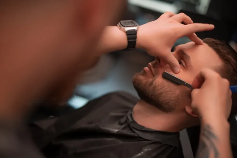Barber goli mężczyznę brzytwą w salonie fryzjerskim